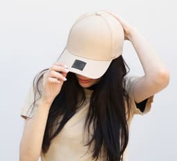 A beige cotton/spandex cap with a branded logo, worn by a person with long hair.