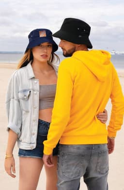 A black and blue bucket hat displayed on a sandy beach, worn by two individuals, one in a yellow hoodie.