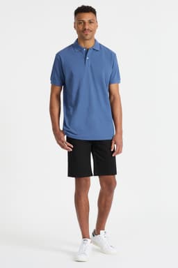 A men's polo shirt in blue, paired with black shorts, displayed on a model. The shirt features a logo.