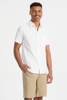 A short-sleeve white button-up shirt with a chest pocket, modelled by a smiling man wearing beige shorts.