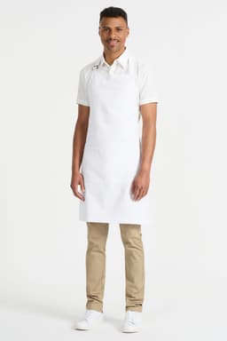 A man wearing a white bib apron stands against a plain background, showcasing the apron’s fit and style.