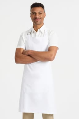 A man wearing a white bib apron stands with arms crossed, featuring a logo on the apron.