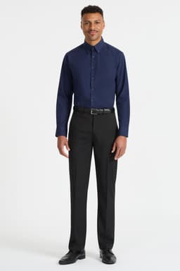 A man stands wearing a navy blue long sleeve button-up shirt and black trousers. The shirt has a logo.