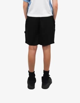Black sports shorts with pockets, featuring a logo, worn by a child standing with hands in pockets.