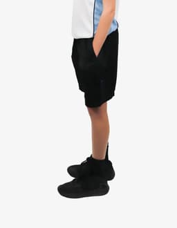 Black sports shorts with pockets, featuring a logo, worn by an individual in a light-coloured top and black shoes.