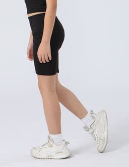 Black girl's legging shorts displayed on a model, paired with white sneakers and ankle socks.