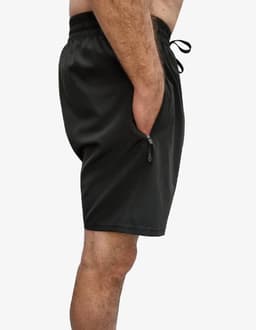 A pair of dark green sports shorts with side pockets and an elastic waistband. Features a logo on the garment.