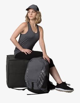 A woman sits on a green box, wearing a grey singlet, black leggings, and a grey cap with a backpack beside her.