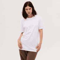 A woman wearing a plain white T-shirt, styled with brown trousers, posing against a neutral background.
