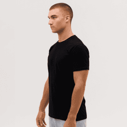 A black T-shirt is displayed on a model standing sideways, featuring a logo on the sleeve.