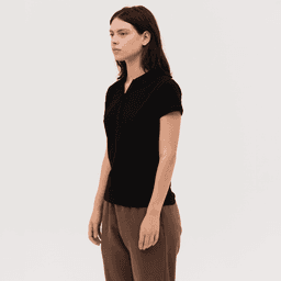 A black women's polo shirt with a zip front and short sleeves, paired with light brown trousers.