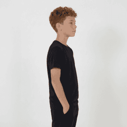 A black youth tee is displayed on a young person standing sideways with hands in pockets.