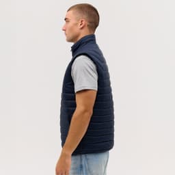 A navy blue puffer vest displayed on a model from the side, featuring a high collar and a sleek design.
