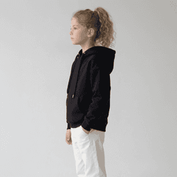 A black youth hoodie with a kangaroo pocket, drawstring hood, and a logo, paired with white trousers.