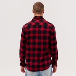 A man is wearing a red and black plaid long sleeve flannel shirt, viewed from the back. The shirt has a collar and buttons.