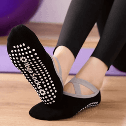 A pair of black yoga socks with grey straps and non-slip grip dots on the soles.