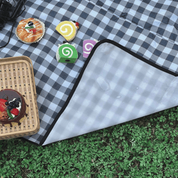 A checkered black and white PVC picnic blanket on grass, featuring desserts and a woven basket.