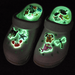 Glow-in-the-dark Croc charms featuring various colourful designs, set against white clogs in a dark background.