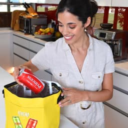 A woman is placing a can inside a bright yellow cooler bag, which features a logo on the front.