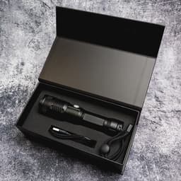 A black rechargeable torch with a charging cable, sitting inside a black box with cushioning.