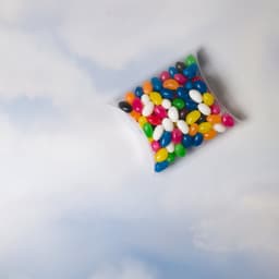 A pillow pack filled with assorted colour mini jelly beans, featuring vibrant hues of green, yellow, blue, pink, and black.