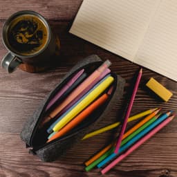 A grey felt utility case filled with colourful pens and pencils, alongside a notepad and a coffee cup.