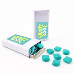 A pack of turquoise chewy mints, with some mints spilled out, in a silver tin featuring a logo.