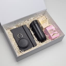A travel mug in black, a notebook, a keyring, and marshmallows in a gift box with shredded fill.