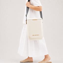 A cream cooler bag carried over the shoulder, featuring a branding logo and set against a neutral background.
