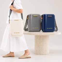 A person carries a white cooler bag, alongside grey and navy cooler bags, all featuring branding.