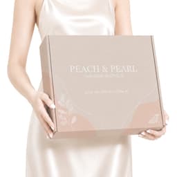 A light beige box with a locking lid, featuring floral motifs and a logo, held by a person in a satin dress.