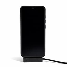 A black phone is displayed on a charger, connected by a charging cable. The charger has a sleek design.