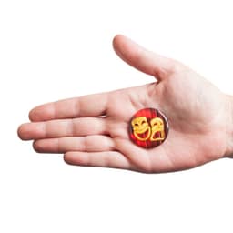 A hand holding a 38mm round magnet featuring two theatrical masks on a red background.