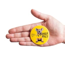 A hand holding a custom printed 64mm round badge featuring a koala design on a bright yellow background.