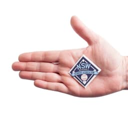 A hand holds a diamond-shaped badge in blue and white with a logo, featuring a baseball design.