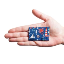 A hand holding a rectangular badge with a colourful nautical design featuring boats, an octopus, and lighthouses.