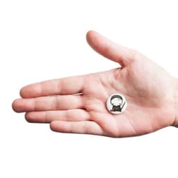 A hand holds a small, custom printed 25mm round magnet featuring a character design. The magnet is primarily white.