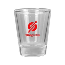 A clear glass shot glass with a solid base and a round logo in red and white.