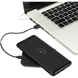 A wireless charging phone stand in black, with a smartphone on it, connected to a laptop by a charging cable.