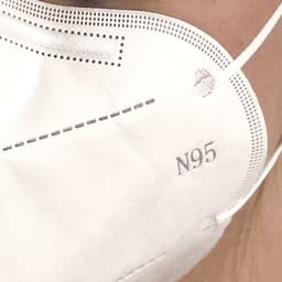 A close-up of a white N95 respirator face mask, featuring a branded logo and a textured surface.