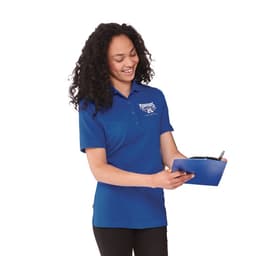 A woman wearing a blue short sleeve polo shirt with a logo, holding a clipboard and smiling.