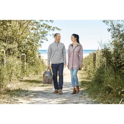 A grey and maroon women's knit zip hoody with a logo, worn with light jeans and brown boots, set against a coastal pathway.