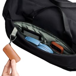 A close-up of a black duffel bag's interior, featuring a blue headset, a gadget, and a brown leather keychain.