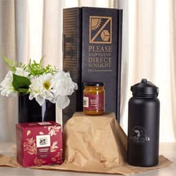 A festive essentials set featuring a black drink bottle, a candle jar, a gift box, and a flower arrangement.