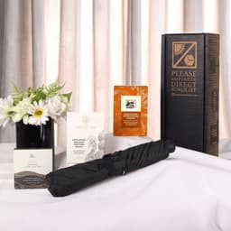 A black umbrella set displayed with assorted product boxes and a floral arrangement on a table.