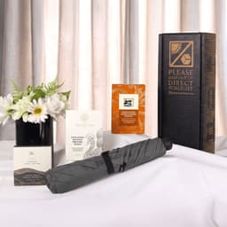 A grey umbrella, flower arrangement, and several boxes with a promotional package, all displayed on a white surface.
