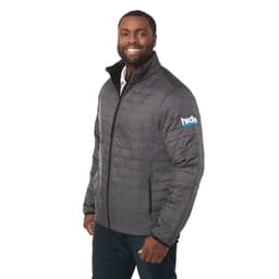 A man wearing a grey insulated puffer jacket with a logo on the sleeve.
