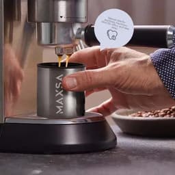 A drink bottle in stainless steel is being filled with liquid from an espresso machine. It features a logo on its side.