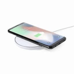 A wireless charging pad with a smartphone placed on it. The pad is circular and appears white.