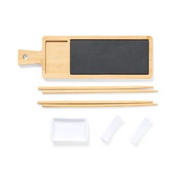 A bamboo serving board with a black slate section, two sets of chopsticks, a small white dish, and two sauce holders.